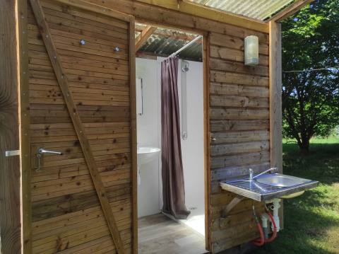 Struttura in legno con porta aperta che mostra un bagno e un lavandino esterno al Camping Domaine La Chabanne.