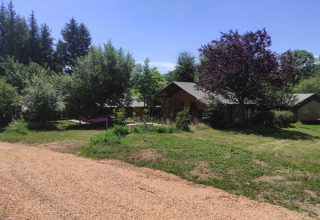 Udsigt over grønne områder og hytter på Camping Domaine La Chabanne i Auvergne-Rhône-Alpes, Frankrig, under en blå himmel.