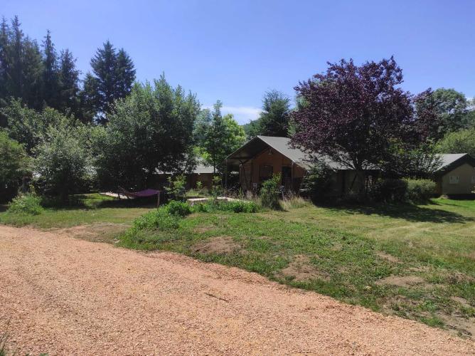 Vue sur les cabanes et paysages verdoyants au Camping Domaine La Chabanne, Auvergne-Rhône-Alpes, France, sous un ciel bleu.