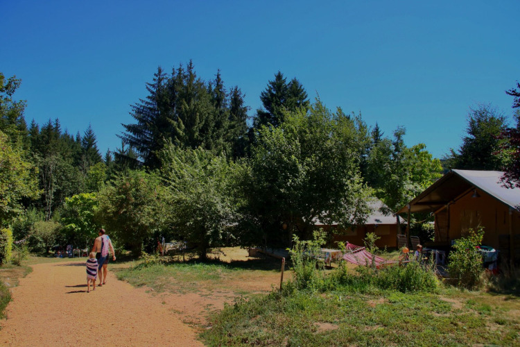 Sonniger Tag in Châtel-Montagne, Frankreich, Menschen spazieren auf einem Weg, umgeben von Bäumen und Hütten.