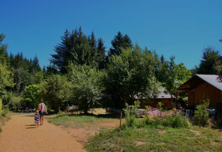 Día soleado en Châtel-Montagne, Francia, con personas caminando por un sendero rodeado de árboles y cabañas.
