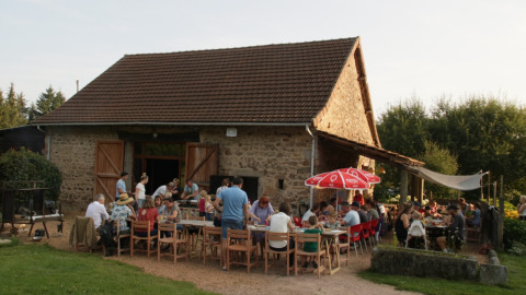 Group enjoying an outdoor meal in front of a stone house at Camping Domaine La Chabanne, Auvergne-Rhône-Alpes, France.