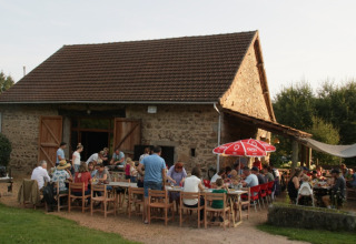 Group enjoying an outdoor meal in front of a stone house at Camping Domaine La Chabanne, Auvergne-Rhône-Alpes, France.