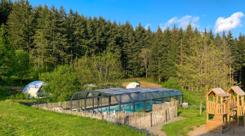 Camping Domaine La Chabanne en Auvergne-Rhône-Alpes con piscina cubierta, área de juegos y un bosque al fondo.