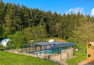 Camping Domaine La Chabanne in Auvergne-Rhône-Alpes featuring a covered pool, playground, and forest backdrop.