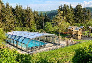 Camping Domaine La Chabanne: Overdækket swimmingpool og legeplads omgivet af grøn natur i Auvergne-Rhône-Alpes.