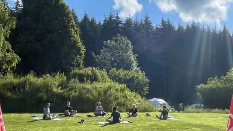 Groep mensen doen aan yoga op het gras bij Camping Domaine La Chabanne, midden in de natuur.