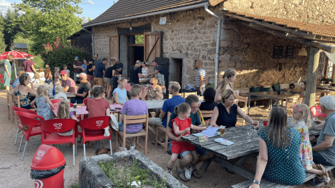 Famiglie e bambini mangiano all'aperto vicino una casa in pietra al Camping Domaine La Chabanne in Francia.