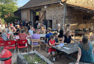 Families and children dining outdoors at rustic stone building at Camping Domaine La Chabanne in France.