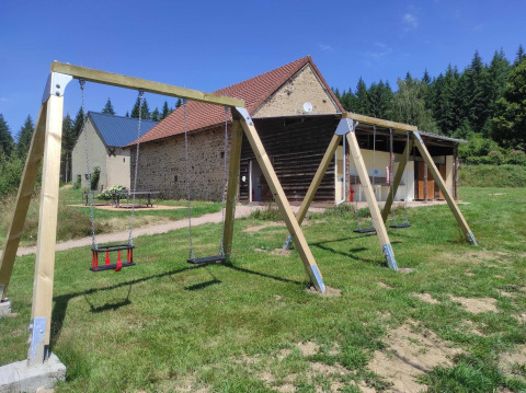 Gynger på legepladsen foran stenbygninger og skov på Camping Domaine La Chabanne i Auvergne-Rhône-Alpes.