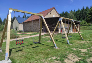 Gynger på legepladsen foran stenbygninger og skov på Camping Domaine La Chabanne i Auvergne-Rhône-Alpes.