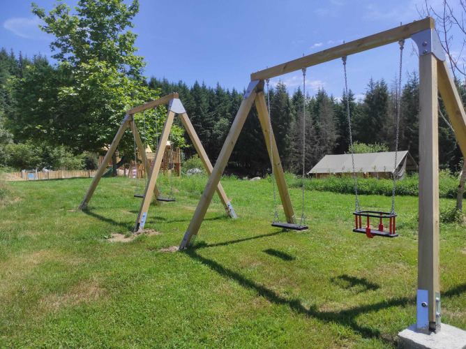 Buitenspeeltuin met houten schommels bij Camping Domaine La Chabanne, Auvergne-Rhône-Alpes, Frankrijk.