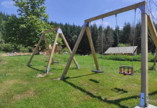 Spielplatz mit Holzschaukeln auf Rasen im Camping Domaine La Chabanne, Auvergne-Rhône-Alpes, Frankreich.