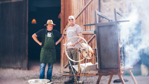 Dos hombres asan carne en un espetón en Camping Domaine La Chabanne, un parque vacacional en Auvergne-Rhône-Alpes, Francia.