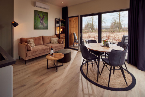 Modern lodge living room with beige sofa, round dining table, large windows, and nature view outside.