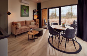 Modern lodge living room with beige sofa, round dining table, large windows, and nature view outside.
