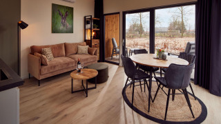 Soggiorno di lodge moderno con divano beige, tavolo rotondo, ampie finestre e vista sulla natura esterna.