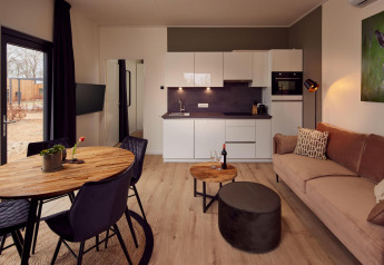 Acogedora sala y cocina de una cabaña moderna con mesa de madera, sofá, vino, plantas y cuadro mural.