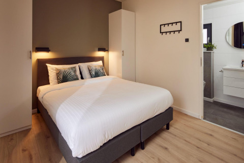 Dormitorio moderno en una cabaña con cama doble, ropa de cama blanca, armario y baño en suite visible.