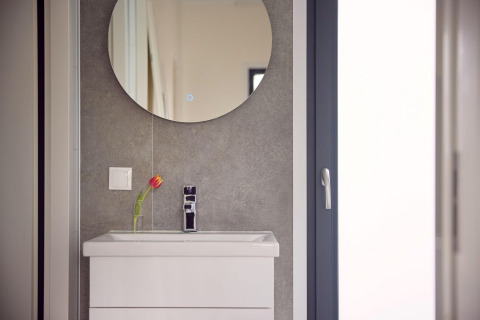 Moderne wastafel met witte kast, ronde spiegel en een tulpenvaas in badkamer van een lodge.