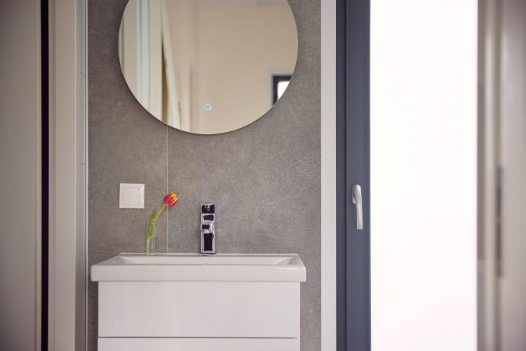 Lavabo moderno con gabinete blanco, espejo redondo y una tulipán en jarrón en el baño de una cabaña.