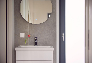 Moderne wastafel met witte kast, ronde spiegel en een tulpenvaas in badkamer van een lodge.