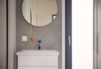 Évier moderne avec armoire blanche, miroir rond et tulipe dans un vase, pris dans un lodge chic.