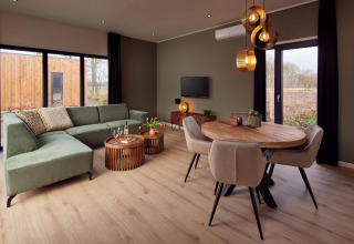 Salon moderne à la Holiday villa Amalia avec canapé vert, coin repas et grandes fenêtres à Hofparken De Bergvennen.