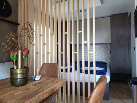 Interior de Tiny House en Kohnenhof, Luxemburgo, con separador de madera, mesa de comedor y dormitorio.