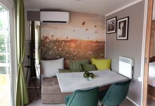 Gezellige eethoek in Tiny House bij Kohnenhof, Luxemburg, met natuurmuurschildering en groene stoelen.