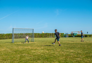 Bambini che giocano a calcio su un prato vicino a Tiny House at Kohnenhof in Lussemburgo sotto un cielo azzurro.