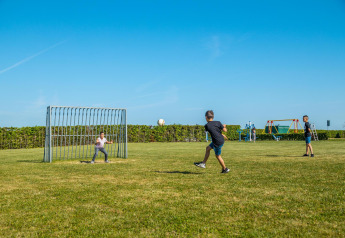 Børn leger fodbold på en grøn mark ved Tiny House at Kohnenhof i Luxembourg under en klar blå himmel.