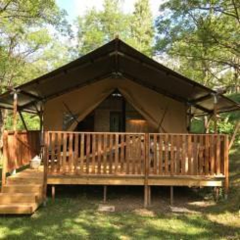 Tienda safari con instalaciones sanitarias en Camping Le Gallo Romain, Francia, rodeada de naturaleza verde.