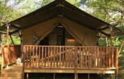 Tienda safari con instalaciones sanitarias en Camping Le Gallo Romain, Francia, rodeada de naturaleza verde.