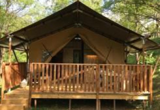Tienda safari con instalaciones sanitarias en Camping Le Gallo Romain, Francia, rodeada de naturaleza verde.