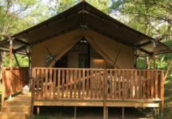 Tienda safari con instalaciones sanitarias en Camping Le Gallo Romain, Francia, rodeada de naturaleza verde.