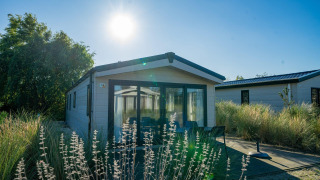Un lodge Velthorst ensoleillé à Poort van Zeeland, Pays-Bas, entouré d’herbes et d’arbustes décoratifs.