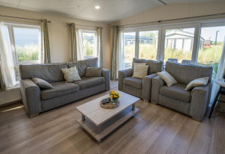 Sala de estar en el lodge Velthorst en Poort van Zeeland, Países Bajos, con sofás grises y grandes ventanales.