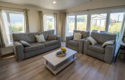 Living room at Velthorst lodge in Poort van Zeeland, Netherlands, with grey sofas, armchairs and large windows.