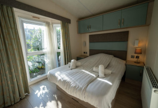 Bedroom of Velthorst lodge at Poort van Zeeland, Netherlands, featuring a double bed, rolled towels, and windows.