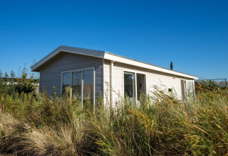 Lodge Velthorst en Poort van Zeeland, Países Bajos, rodeado de hierbas altas bajo un cielo azul claro.