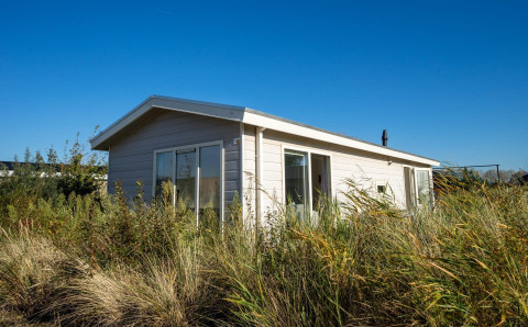 Modern Velthorst lodge at Poort van Zeeland in the Netherlands, surrounded by tall grasses under a blue sky.
