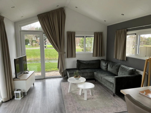 Sala moderna en la cabaña Velthorst en Poort van Zeeland, Países Bajos, con sofá gris y vista al jardín.