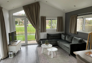 Sala moderna en la cabaña Velthorst en Poort van Zeeland, Países Bajos, con sofá gris y vista al jardín.