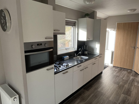 Cocina moderna blanca en una cabaña Velthorst en Poort van Zeeland, Países Bajos, con horno y estufa.