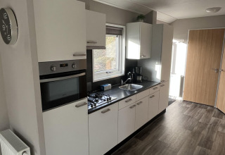 Cocina moderna blanca en una cabaña Velthorst en Poort van Zeeland, Países Bajos, con horno y estufa.