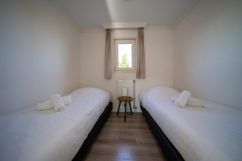 Schlafzimmer mit zwei Einzelbetten, einem kleinen Tisch und Fenster in der Velthorst-Lodge, Poort van Zeeland.