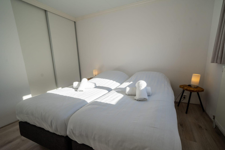 Dormitorio con dos camas individuales y sábanas blancas en la cabaña Velthorst de Poort van Zeeland, Países Bajos.