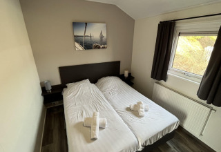 Chambre avec deux lits simples, rideaux foncés, fenêtre et tableau de voiliers, située au Velthorst lodge.