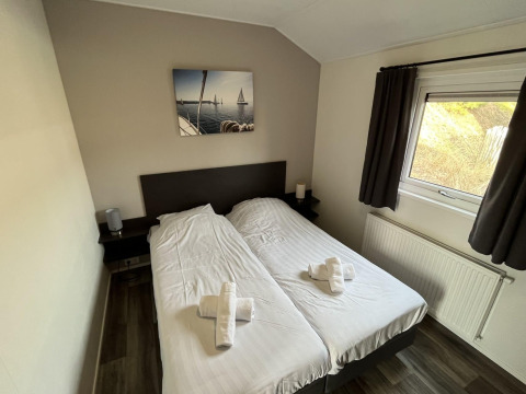 Chambre avec deux lits simples, rideaux foncés, fenêtre et tableau de voiliers, située au Velthorst lodge.